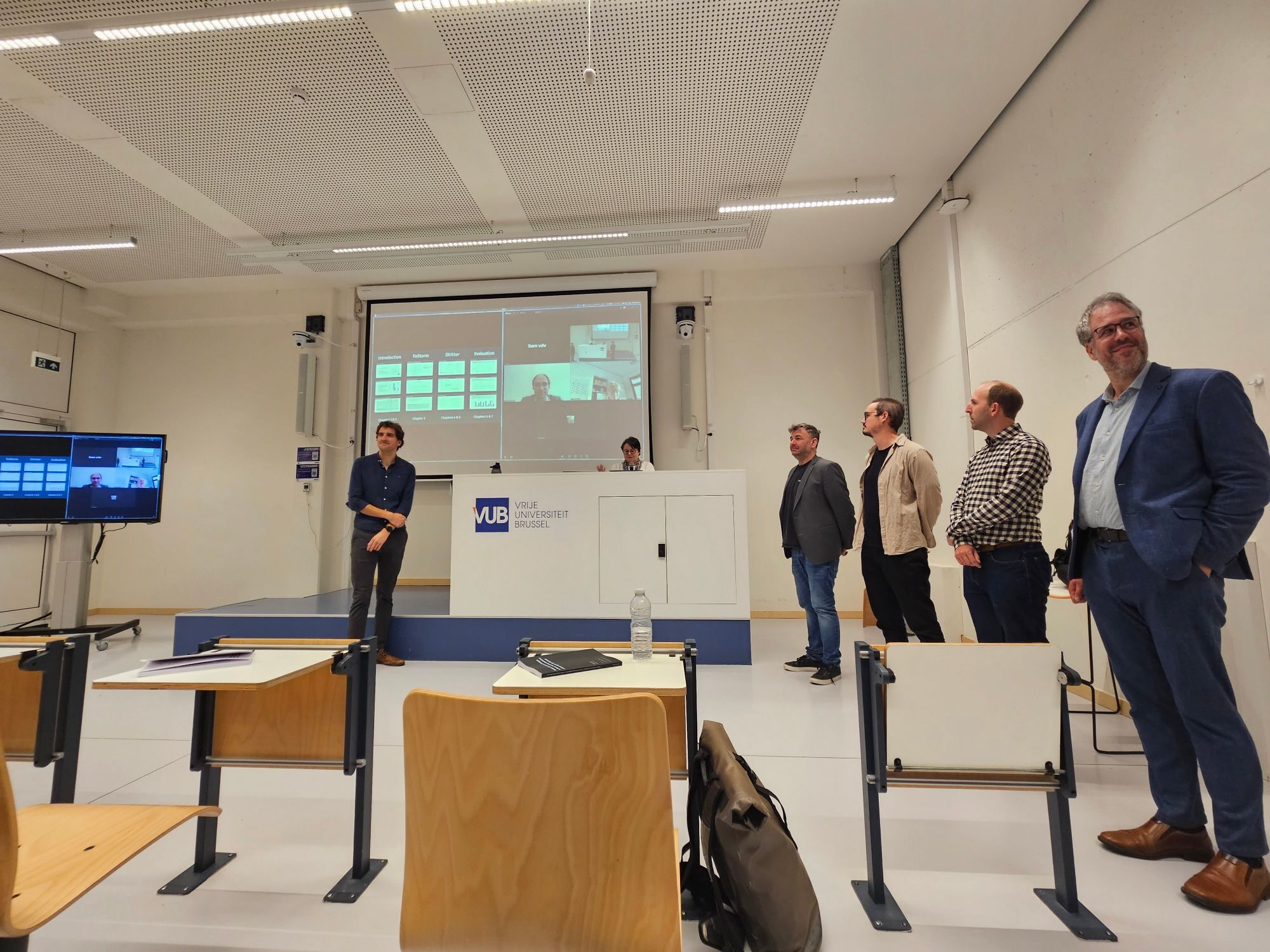 Mathijs Saey's public PhD defence in a VUB lecture room, with the presentation and jury members joining online on the screen behind him