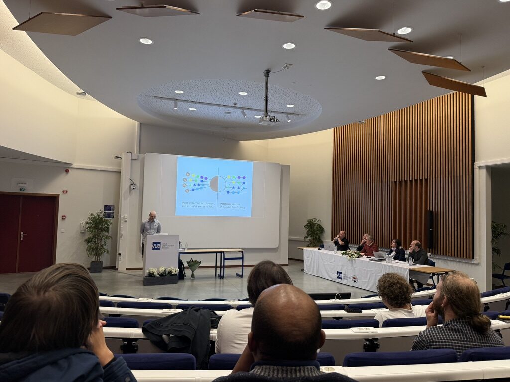 Tim Baccaert presenting his PhD defence in a VUB auditorium, with the jury seated at a table to the right of the screen
