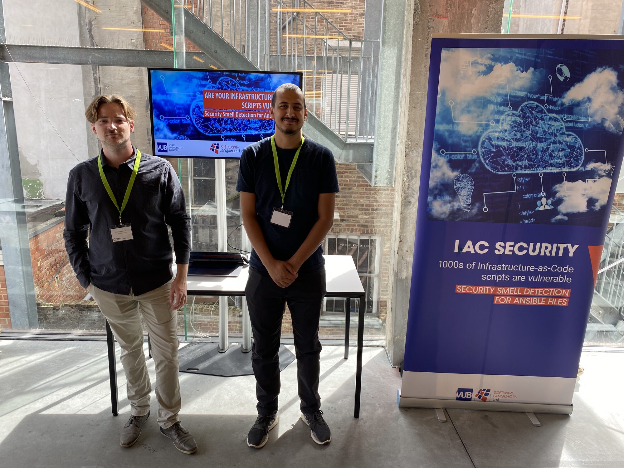 Two SOFT researchers at a booth on Infrastructure as Code security, next to a screen on security smell detection for Ansible scripts